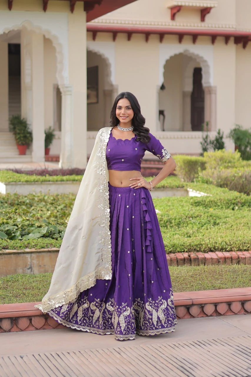 Woman in a purple traditional outfit standing in front of a building with greenery.